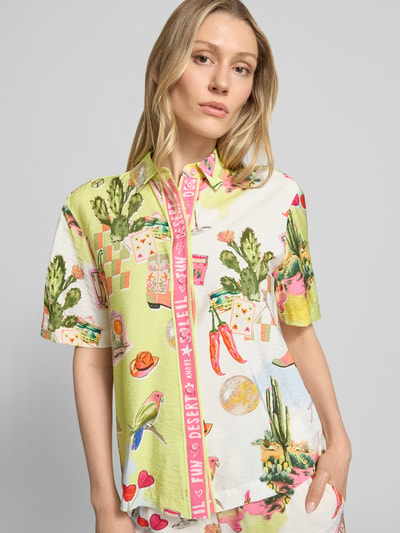 Frauenmodel trägt Bluse aus Viskose-Mix mit abgerundetem Saum von Marc Cain; buntes Muster, Kentkragen, Knopfleiste, Straight Fit, Ganzkörperansicht von vorne, Rückenlänge bei Größe 36: 61 cm, Ärmellänge bei Größe 36: 25 cm.