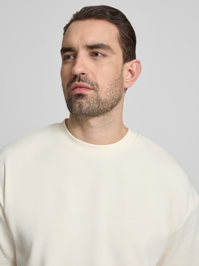 Männermodel trägt Oversized T-Shirt mit Rundhalsausschnitt von Lindbergh aus Baumwoll-Mix, Label-Detail, helle Farbe, Nahaufnahme Oberkörper. Rückenlänge bei Größe M: 70 cm.