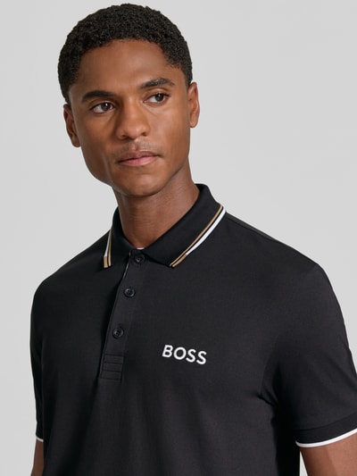 Mężczyzna model nosi czarną koszulkę polo Regular Fit Poloshirt aus Baumwoll-Mix model 'Paddy Pro' od BOSS Green, zbliżenie na górną część ciała.