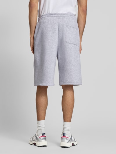 Męski model nosi Sweatshorts mit Logo-Print od REVIEW, mieszanka bawełny, krój loose fit, elastyczny pas, szary, długość wewnętrzna nogawki 28 cm, szerokość w rozmiarze M 45 cm. Ganzkörperansicht Rückansicht.