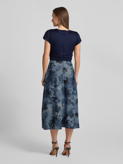 Vrouwenmodel draagt Maxikleid mit floralem Print van Swing, blauw-wit elastisch materiaal, getailleerde pasvorm, bloemenprint, V-hals, korte mouwen, naadrits, ruglengte 136 cm, borstbreedte 16 cm, mouwlengte 5 cm. Volledige lichaamsweergave van achteren.