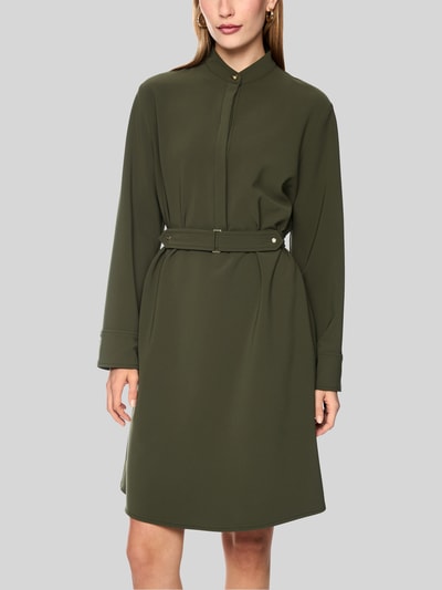 Frauenmodel trägt Knielanges Kleid mit Stehkragen und Gürtel von Marc Cain in Olivgrün, glatte Textur, taillierter Schnitt, Nahaufnahme Oberkörper, Material-Mix mit Stretch-Anteil, Ganzkörperansicht von vorne.