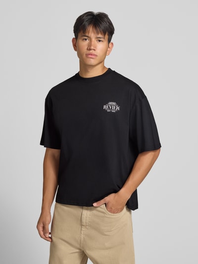 Männermodel trägt Regular Fit T-Shirt aus reiner Baumwolle mit rückseitigem Print von REVIEW in Schwarz, Logo-Detail, Nahaufnahme Oberkörper. Rückenlänge bei Größe M: 67 cm.