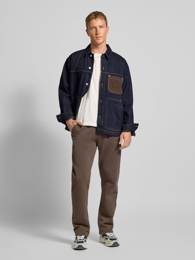 Männermodel trägt Regular Fit Jeansjacke aus reiner Baumwolle von Tommy Jeans in Melange-Optik, Denim, Logo-Stitching, Ganzkörperansicht von vorne.