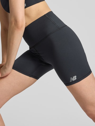 Frauenmodel trägt Radlerhose mit Logo und elastischem Bund von New Balance aus schwarzem Material-Mix mit Stretch-Anteil, Nahaufnahme Oberschenkel.