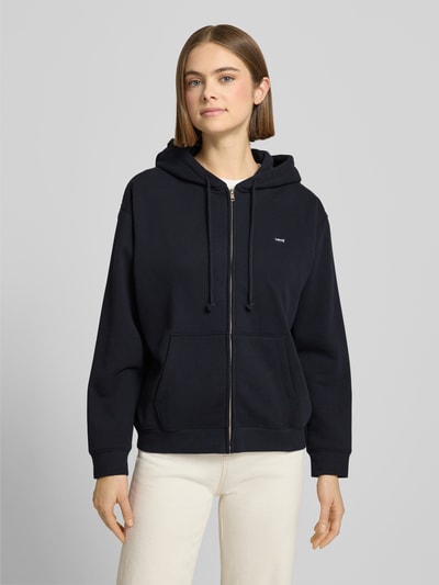 Kobiece modelka nosi czarną Sweatjacke mit Reißverschluss von Levi's®, luźny krój, kaptur, kieszenie, przód, bawełniany miks, ujęcie całej sylwetki z przodu.