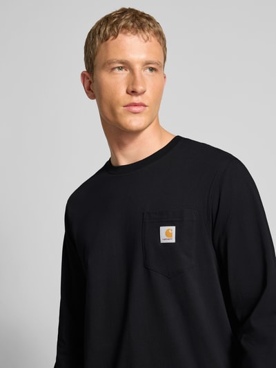 Männermodel trägt Longsleeve mit Brusttasche und Label-Detail von Carhartt Work In Progress aus Reine Baumwolle, Regular-Fit, Rundhalsausschnitt, Nahaufnahme Oberkörper.