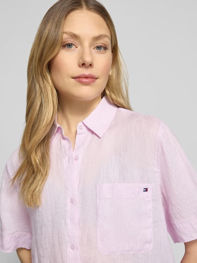 Modelka kobieca ma na sobie Regular Fit Leinenbluse mit Logo-Stitching od Tommy Hilfiger, efekt: jednolity kolor, krój regular fit, kołnierzyk koszulowy, wyhaftowane logo, pas na plecach z zakładką, listwa guzikowa, krótki rękaw, brustasza, materiał: czysty len. Zbliżenie na górną część ciała.