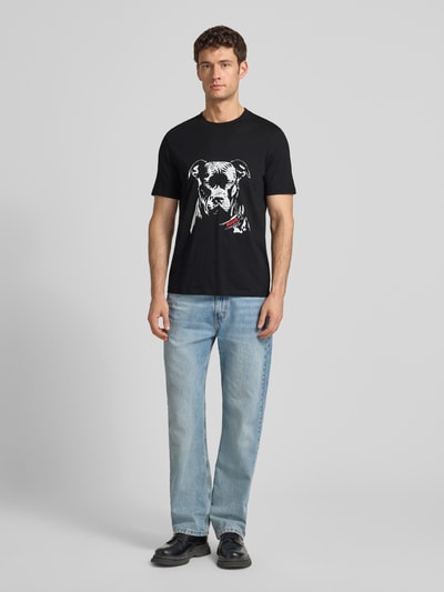 Männermodel trägt Regular Fit T-Shirt aus reiner Baumwolle Modell 'DUBROX' von HUGO in Schwarz mit Motiv-Print, Ganzkörperansicht von vorne.