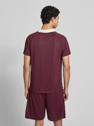 Männermodel trägt Regular Fit T-Shirt mit Logo-Stitching Modell 'Heritage' von KARL KANI in Weinrot mit Umlegekragen, Rückenlänge 70 cm, Ganzkörperansicht Rückansicht.