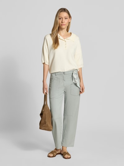 Modelka nosi Relaxed Fit Jeans aus Lyocell-Mix von Cambio, mieszanka lyocellu i bawełny, zapięcie na guzik i zamek błyskawiczny, wpuszczane i tylne kieszenie, szlufki na pasek z chustą, skrócony krój, szerokość w rozmiarze 36: 41 cm, długość wewnętrzna nogawki w rozmiarze 36: 69 cm, jasnoszary kolor, gładka faktura, widok całej sylwetki z przodu.