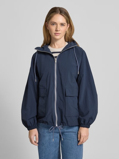 Modelka kobieca ma na sobie Jacke mit Kapuze und Pattentaschen od Jake*s Casual w kolorze granatowym, relaxed fit, kaptur z troczkiem, zamek błyskawiczny, patkowe kieszenie, szerokość w rozmiarze 36: 56 cm, szerokość ramion: 41 cm, długość tyłu: 66 cm, długość rękawa: 65 cm, widok całej sylwetki z przodu