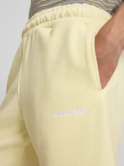 Männermodel trägt Relaxed Fit Shorts mit Strukturmuster Modell 'Lagos' von Pegador in Hellgelb, elastischer Bund, Nahaufnahme Oberkörper, elastischer Material-Mix.