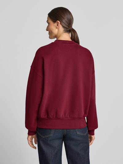 Frauenmodel trägt Oversized Sweatshirt aus reiner Baumwolle Modell 'ALIZAA' von ARMEDANGELS in Dunkelrot, glatte Textur, Ganzkörperansicht Rückansicht.