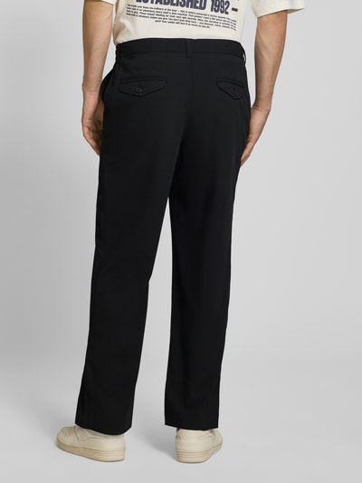 Męski model nosi Regular Fit Bundfaltenhose mit Gesäßtaschen od REVIEW, czarny kolor, Mieszanka materiałów z dodatkiem wiskozy, zakładki w pasie, kieszenie z tyłu, szerokość w rozmiarze M: 46 cm, długość wewnętrzna nogawki w rozmiarze M: 78 cm, zdjęcie całych spodni od tyłu