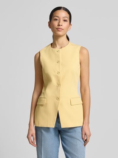 Frauenmodel trägt Weste aus Lyocell-Baumwoll-Mix mit Pattentaschen von Scotch & Soda in Gelb, taillierter Schnitt, Rundhalsausschnitt, Knopfleiste, Rückenlänge bei Größe S 66 cm, Schulterbreite 35 cm, Brustweite 44 cm, Ganzkörperansicht von vorne.