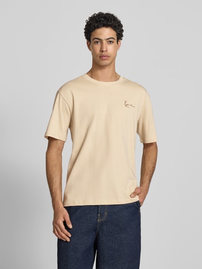 Männermodel trägt Relaxed Fit T-Shirt mit Logo-Stitching von KARL KANI, Herren T-Shirt aus Reine Baumwolle, Rundhalsausschnitt, beige, Ganzkörperansicht von vorne. Rückenlänge bei Größe M: 65 cm.