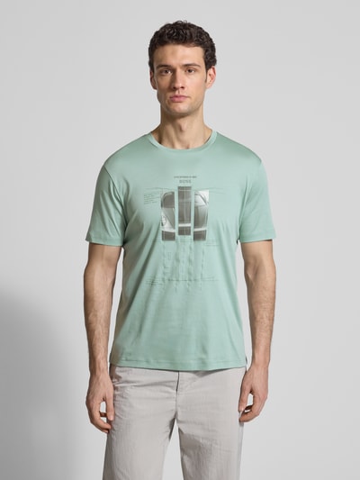 Männermodel trägt Regular Fit T-Shirt aus reiner Baumwolle Modell 'SPIRIT70' von BOSS Green x Porsche in Mintgrün mit Motiv-Print, Ganzkörperansicht von vorne.