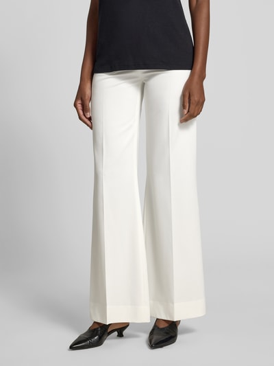 Frauenmodel trägt Flared Fit Stoffhose aus Woll-Mix von Victoria Beckham in Weiß mit Bundfalten und aufgesetzten Eingrifftaschen, Nahaufnahme Unterkörper.