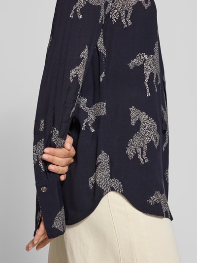 Frauenmodel trägt Relaxed Fit Bluse aus reiner Viskose Modell 'ODETTA' von ODETTA, dunkelblau mit weißem Allover-Motiv-Print, Zierschleife, langärmeliges Design, strukturierte Stoffoberfläche, Nahaufnahme Oberkörper.