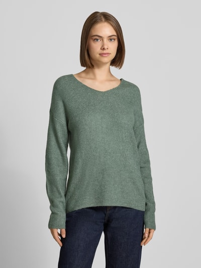 Frauenmodel trägt Regular Fit Pullover mit V-Ausschnitt Modell 'CAMILLA' von ONLY, grün meliert, grobe Strickstruktur, Ganzkörperansicht von vorne, Damen Pullover von ONLY.