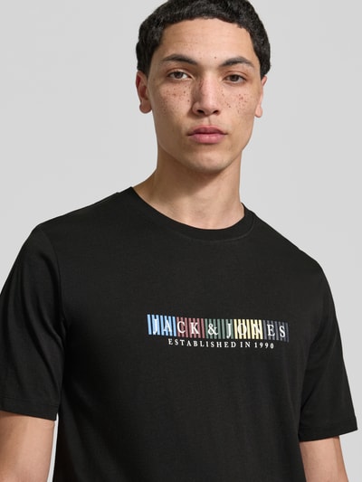 Männermodel trägt schwarzes T-Shirt aus Bio-Baumwolle Modell 'NANTUCKET' von Jack & Jones mit Label-Print, Nahaufnahme Oberkörper.
