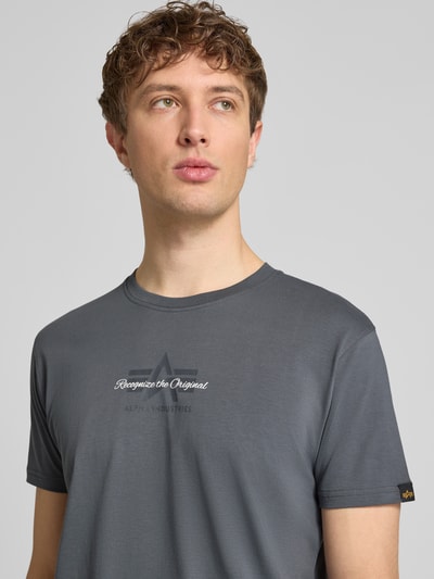 Męski model nosi T-Shirt mit Label-Detail od Alpha Industries z czystej bawełny, prosty krój, okrągły dekolt, detal z logo, widok na górną część tułowia z przodu.