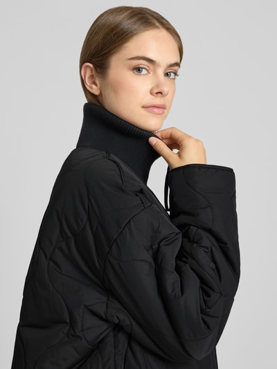Vrouwenmodel draagt zwarte gewatteerd jack met doorgestikte naden, gebreide opstaande kraag en steekzakken, Model 'SERENA' van JJXX, loose fit, ritssluiting, Nahaufnahme Oberkörper.