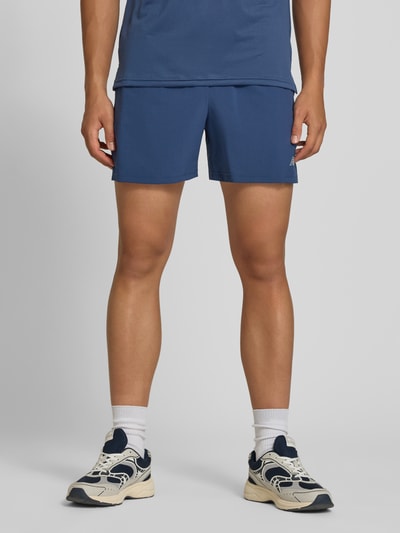 Männermodel trägt Shorts mit elastischem Bund und Logo von New Balance, Regular Fit, Tunnelzug, blau, Nahaufnahme Unterkörper, Vorderansicht.