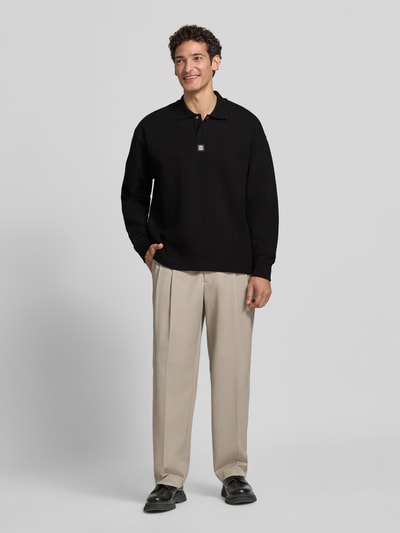 Męski model nosi Oversize Fit Sweatshirt aus Baumwoll-Mix model 'Dabins' od HUGO w kolorze czarnym, neutralne beżowe spodnie, gładka faktura materiału, Ganzkörperansicht von vorne.