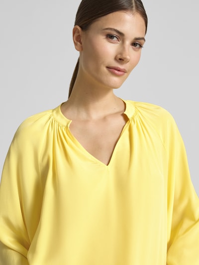 Kobieta nosi Regular Fit Bluse mit V-Ausschnitt von HERZENS, żółty, tunikowy kołnierz, lejący materiał, zbliżenie górnej części ciała.