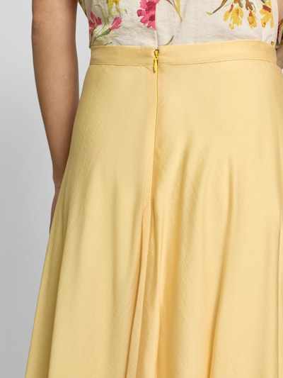 Vrouwenmodel draagt Midirock mit rückseitigem Reißverschluss van Jake*s Collection in lichtgeel satijn, a-lijn, detailopname taille en rits.