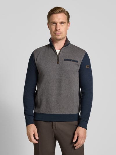 Männermodel trägt Sweatshirt mit Label-Details von bugatti in Grau und Dunkelblau, Troyer-Kragen, Brusttasche, Ganzkörperansicht von vorne. Elastischer Material-Mix mit Baumwoll-Anteil, gerader Schnitt, Rückenlänge 64 cm, Ärmellänge 66 cm.