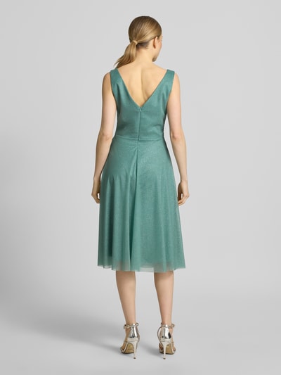 Frauenmodel trägt Knielanges Cocktailkleid mit V-Ausschnitt von TROYDEN COLLECTION aus grünem Chiffon, Taillierter Schnitt, Knielänge, Breite Träger, Rückseitiger V-Ausschnitt, Rückenreißverschluss, Rückenlänge 85 cm, Brustweite 43 cm, Ganzkörperansicht Rückansicht.