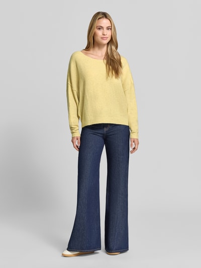 Frauenmodel trägt Relaxed Fit Strickpullover aus Material-Mix mit Leinen-Anteil von American Vintage in Gelb, Damenpullover mit gerippten Abschlüssen, überschnittenen Schultern und Rundhalsausschnitt, kombiniert mit blauer Schlaghose, Ganzkörperansicht von vorne.