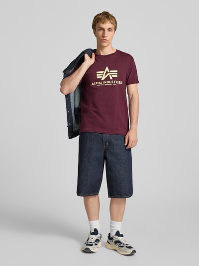 Mężczynamodel trägt T-Shirt mit Logo und Rundhalsausschnitt von Alpha Industries, bawełna, krój regular fit, logo, długość tyłu w rozmiarze M: 68 cm, widok całej sylwetki z przodu