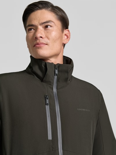 Männermodel trägt Regular Fit Jacke mit Logo-Print von Lindbergh, elastyczna mieszanka materiałów, kolor ciemnozielony, nadruk z logo, detal napoleońskiej kieszeni, Nahaufnahme górnej części ciała. Szerokość ramion w rozmiarze M: 46 cm, Szerokość klatki piersiowej w rozmiarze M: 42 cm, Długość rękawów: 62 cm, Długość tyłu: 74 cm.