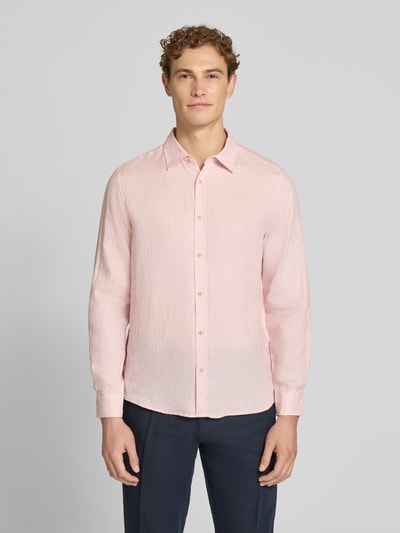 Męskamodel nosi Regular Fit Freizeithemd aus reinem Leinen od s.Oliver RED LABEL w jasnoróżowym kolorze, gładka faktura, krój regular fit, długi rękaw, kołnierzyk kent, zapięcie na pojedynczy rząd guzików, mankiety, logo-patch, wykonana z czystego lnu; widok całej sylwetki z przodu.