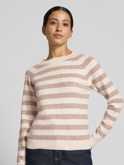 Modelka kobieca ma na sobie sweter Regular Fit Pullover mit Streifen model 'DOFFY' od VERO MODA, beżowe i kremowe paski, widok całej sylwetki z przodu.