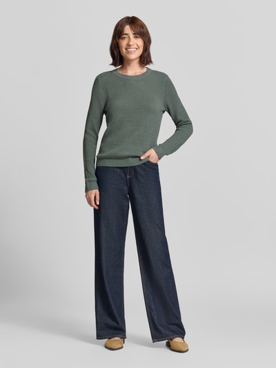 Modelka nosi sweter z dzianiny ze strukturą i okrągłym dekoltem od VILA, bawełna, krój slim fit, fakturowany wzór, Model 'dalo', Długość tyłu 60 cm, Długość rękawów 65 cm, ciemnozielony, szerokie jeansy, beżowe buty, zdjęcie całej sylwetki z przodu.