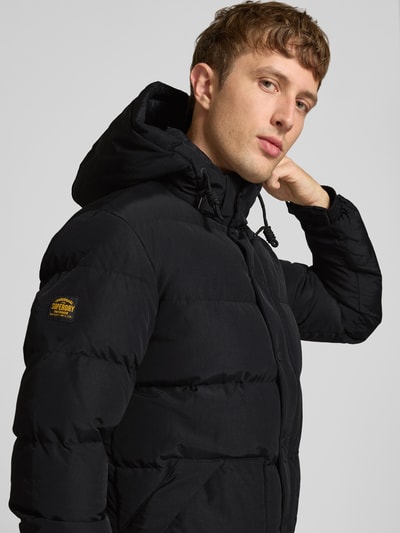 Männermodel trägt zwarte Heren jack met capuchon, recht model, labelpatch, steekzakken, Model 'CLASSIC EVEREST' van Superdry, Nahaufnahme Oberkörper.