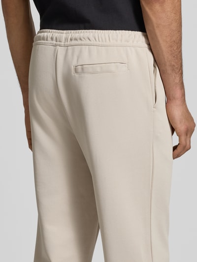 Männermodel trägt Spodnie dresowe z mieszanki bawełny Pegador, model 'Motus Track Pants' w kolorze beżowym, wyhaftowane logo, kieszeń z tyłu, krój regular fit, długość wewnętrzna nogawki w rozmiarze M: 73 cm, widok z tyłu, zbliżenie na biodra.