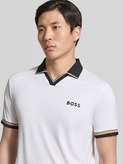 Mężczyzna nosi koszulkę polo Slim Fit Poloshirt mit Label Print model 'PL_TOC SERVE 2' od BOSS Green, efekt: jednolity kolor, krój regular fit, paski w kontrastowym kolorze, kołnierzyk polo, rękaw: krótki rękaw, zakończenie rękawów: prążkowane, zbliżenie na górną część ciała