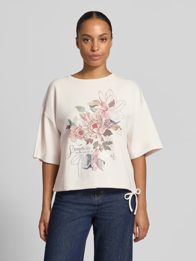 Frauenmodel trägt Relaxed Fit T-Shirt mit Statement-Print von Christian Berg Woman, florales Muster, helles Rosa, weich fallender Stoff, Ganzkörperansicht von vorne. Damen T-Shirt, elastischer Material-Mix mit Modal-Anteil, 1/2-Arm.