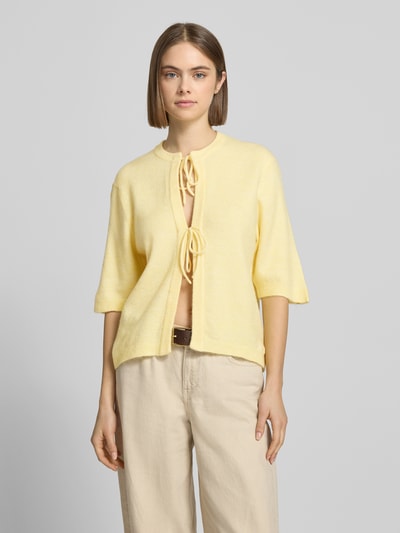 Kobiece modelka nosi Regular Fit Cardigan mit Schnürungen Modell 'SIMONI' od Only, żółty, dzianinowa faktura, półrękaw, okrągły dekolt, prosta forma, widok całej sylwetki z przodu.