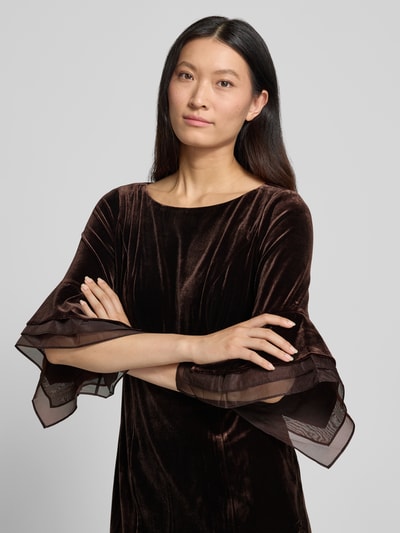 Frauenmodel trägt Abendkleid aus Samt mit Rundhalsausschnitt von Adrianna Papell in Braun, taillierte Passform, Nahaufnahme Oberkörper. Material-Mix mit Stretch-Anteil, feine Textur, rückseitiger Reißverschluss, lange Ärmel.