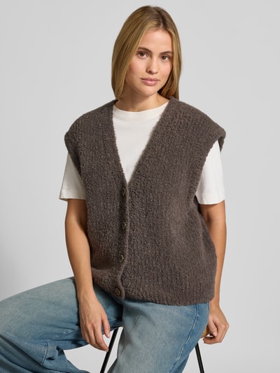 Modelka nosi kamizelkę Relaxed Fit Weste mit Alpaka-Anteil Modell 'Zolly' von American Vintage z mieszanki bawełny i wełny z alpaki, imitacja dzianiny, listwa guzikowa, dekolt w serek, długość tyłu w rozmiarze XS/S: 57 cm, widok na górną część sylwetki z przodu.