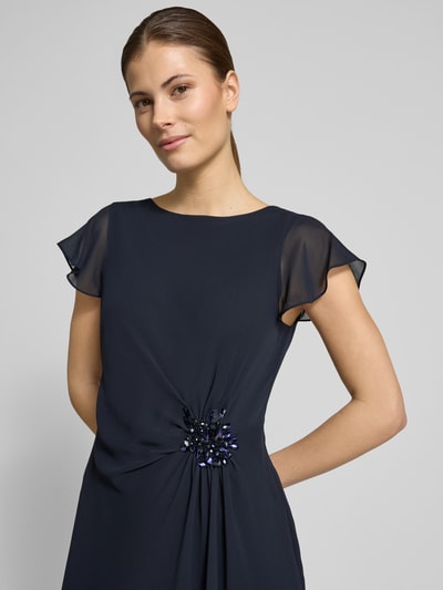 Frauenmodel trägt Knielanges Cocktailkleid mit Ziersteinbesatz von Christian Berg Cocktail in Dunkelblau, Chiffon, taillierter Schnitt, Rundhalsausschnitt, Ziersteinbesatz, Nahaufnahme Oberkörper.