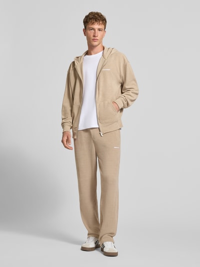 Männermodel trägt Wide Fit Sweatpants mit Label-Detail Modell 'Mezzano' von PEGADOR in Beige mit Eingrifftaschen, Ganzkörperansicht von vorne. Elastischer Material-Mix, elastischer Bund, Innenbeinlänge Größe M 78 cm.