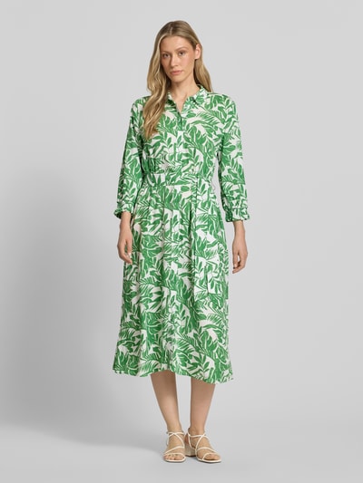 Modelka kobieca ma na sobie „Midikleid aus reiner Viskose mit Umlegekragen” od More & More, zielono-biały, florystyczny print, krój taliowany, pasek, półrękaw, guziki na całej długości, elastyczne mankiety, długość tyłu w rozmiarze 36: 125 cm, szerokość w rozmiarze 36: 40 cm, długość rękawa w rozmiarze 36: 49 cm; widok całej sylwetki z przodu.